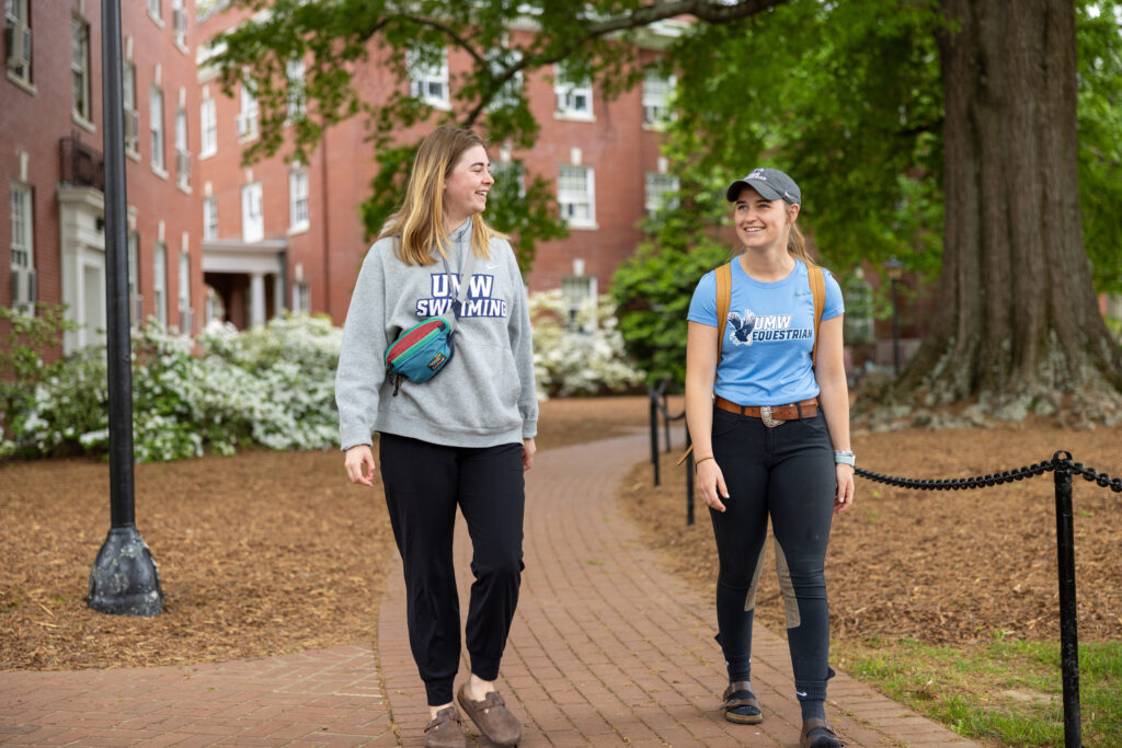 Two young college chat with each other as they walk down a brick sidewalk.